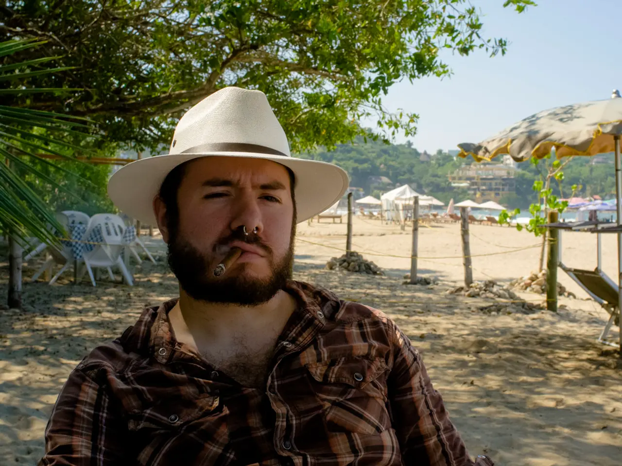 This picture is clicked outside. In the foreground we can see a man wearing shirt, hat and seems to...