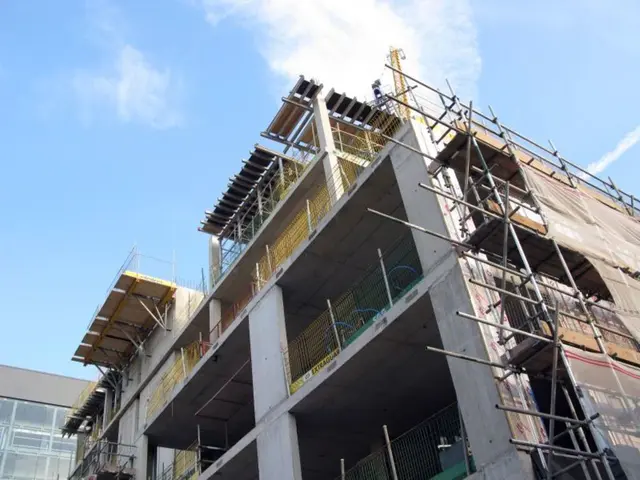 In the image we can see there are buildings and there are iron rods. There is a cloudy sky.