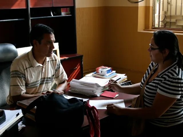 In this picture there is a man who is wearing a cream t shirt is sitting on the chair. To the...