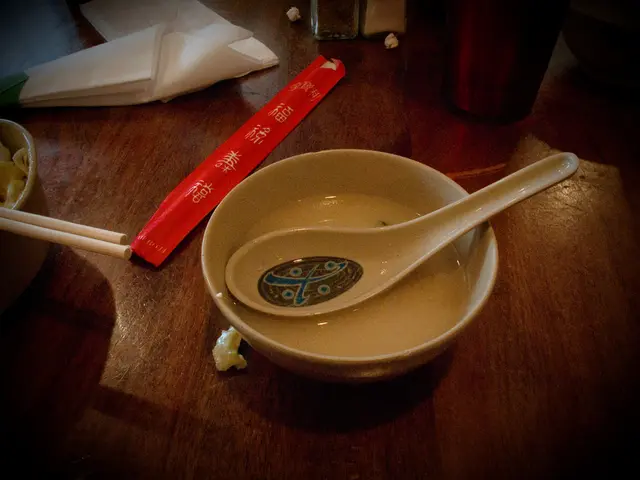 Here we can see a bowl of soap which is placed on a table and beside that there is a cup of noodles...